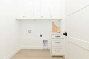 Washroom featuring hookup for an electric dryer, washer hookup, light wood-style floors, and cabinet space