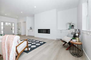 Living room with light wood-type flooring, recessed lighting, and a glass covered fireplace