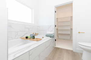 Primary bathroom featuring light wood-style flooring, a bath, and a spacious closet