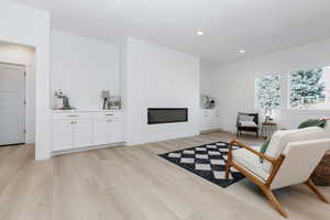 Living room with recessed lighting, light wood-style floors, and a glass covered fireplace