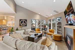 Living room with a glass covered fireplace, recessed lighting, plenty of natural light, and high vaulted ceiling