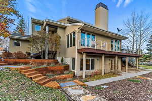 Rear view of house featuring stairway, stucco siding, a chimney, and a deck