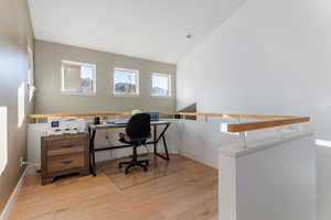 Home office with light wood-style flooring and high vaulted ceiling