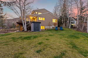 Back of house at dusk featuring stairs, stucco siding, a lawn, and a wooden deck