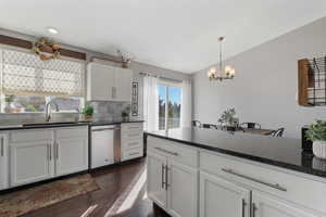 Kitchen featuring white cabinetry, dark wood-style floors, stainless steel dishwasher, dark stone countertops, and tasteful backsplash