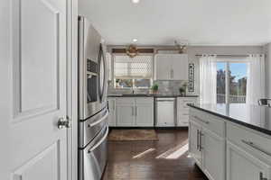Kitchen with tasteful backsplash, appliances with stainless steel finishes, white cabinets, dark wood finished floors, and dark stone countertops