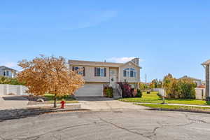 Bi-level home featuring concrete driveway, a chimney, a garage, and stairs
