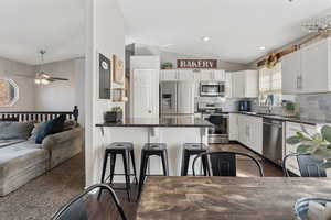 Kitchen featuring lofted ceiling, stainless steel appliances, white cabinetry, dark stone countertops, and tasteful backsplash