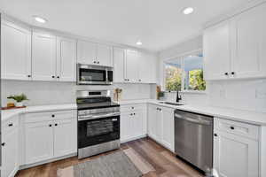 Kitchen with appliances with stainless steel finishes, white cabinets, light wood finished floors, backsplash, and recessed lighting