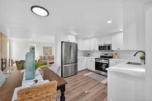 Kitchen featuring appliances with stainless steel finishes, white cabinetry, light wood-style floors, decorative backsplash, and light stone countertops