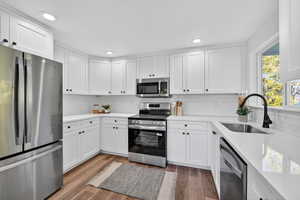 Kitchen featuring stainless steel appliances, white cabinetry, dark wood-type flooring, light stone counters, and recessed lighting