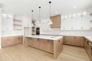 Kitchen featuring open shelves, glass insert cabinets, decorative backsplash, a large island, and light wood-style floors