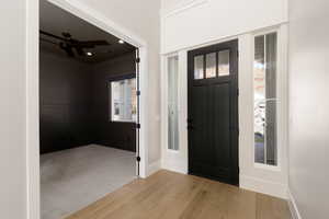 Entrance foyer with ornamental molding, light wood-type flooring, a ceiling fan, light carpet, and a decorative wall