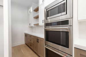 Kitchen with glass insert cabinets, brown cabinets, appliances with stainless steel finishes, white cabinetry, and light wood finished floors