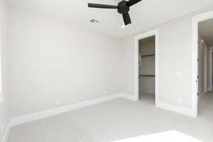 Unfurnished bedroom with light colored carpet, a walk in closet, a ceiling fan, and recessed lighting