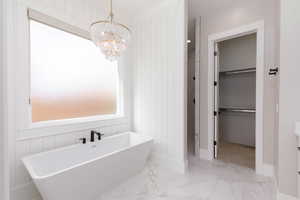 Bathroom featuring light marble finish floors, a freestanding bath, a shower stall, wood walls, and a spacious closet