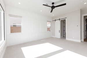 Unfurnished bedroom featuring light carpet, a barn door, a decorative wall, recessed lighting, and ceiling fan