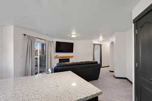Kitchen with light carpet, arched walkways, light stone counters, open floor plan, and a fireplace