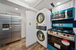 Kitchen featuring stainless steel appliances, dark wood-type flooring, white cabinets, recessed lighting, and stacked washing machine and dryer
