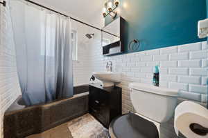 Bathroom featuring shower / bathtub combination with curtain, vanity, and tile walls