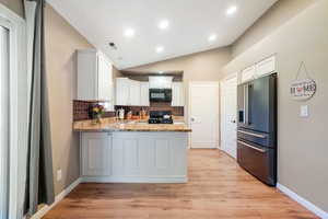 Kitchen featuring backsplash, white cabinets, black appliances, vaulted ceiling, and light wood-style flooring