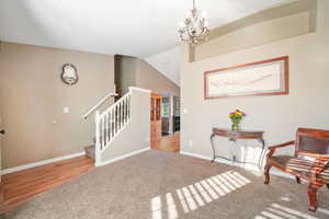 Living area featuring carpet, vaulted ceiling, stairway, a chandelier, and wood finished floors