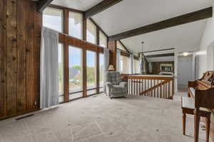 Living area with beamed ceiling, high vaulted ceiling, carpet, an upstairs landing, and wooden walls
