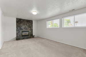 Unfurnished living room with a fireplace, a textured ceiling, and light carpet