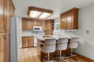 Kitchen featuring open shelves, white appliances, light wood-style floors, brown cabinets, and backsplash