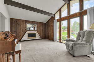 Sitting room with wooden walls, beamed ceiling, carpet floors, high vaulted ceiling, and a fireplace