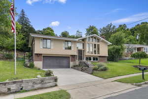 Split foyer home featuring brick siding, stucco siding, driveway, an attached garage, and a chimney