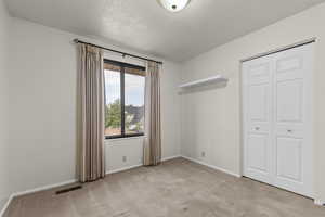 Unfurnished bedroom with light carpet, a textured ceiling, and a closet