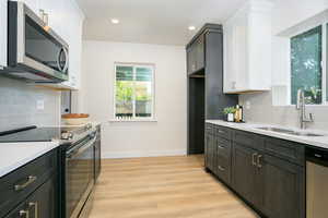 Kitchen with tasteful backsplash, stainless steel appliances, white cabinets, light stone countertops, and light wood-type flooring