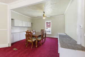 Dining room with a textured ceiling, dark colored carpet, crown molding, and ceiling fan