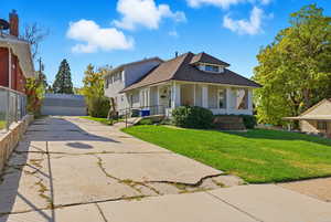 View of front facade with covered porch, a shingled roof, a front lawn, and an outdoor structure