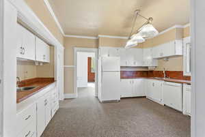Kitchen with white appliances, ornamental molding, white cabinets, pendant lighting, and dark colored carpet