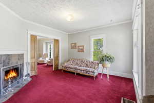 Sitting room featuring ornamental molding, a textured ceiling, a tiled fireplace, and carpet floors