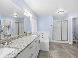 Bathroom featuring a bath, double vanity, a stall shower, and light tile patterned floors