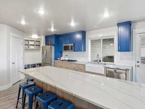 Kitchen featuring blue cabinets, light wood-style flooring, light stone countertops, appliances with stainless steel finishes, and recessed lighting