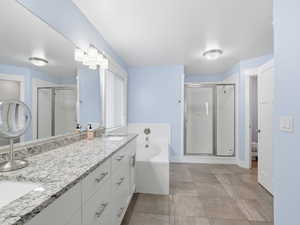 Bathroom featuring a garden tub, double vanity, a shower stall, and light tile patterned floors