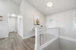 Hallway with light wood-style flooring and high vaulted ceiling