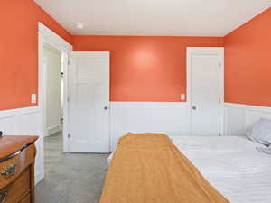 Bedroom featuring a decorative wall, wainscoting, and carpet flooring