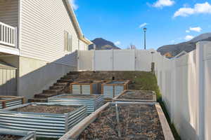 Fenced backyard with a mountain view, a patio area, stairs, and a vegetable garden