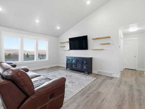 Living room with high vaulted ceiling, light wood-style floors, and recessed lighting