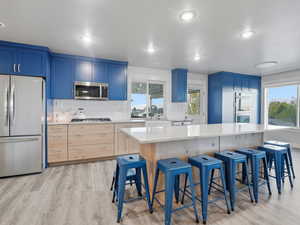 Kitchen with a kitchen breakfast bar, appliances with stainless steel finishes, blue cabinetry, light stone counters, and recessed lighting