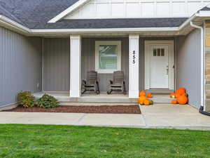 Entrance to property with a shingled roof, covered porch, stone siding, and a lawn