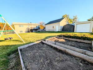 View of grassy yard featuring a playground, an outbuilding, and a garden