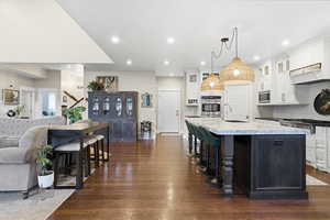 Kitchen featuring backsplash, a breakfast bar, hanging light fixtures, white cabinetry, and a kitchen island with sink