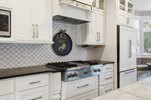 Kitchen featuring backsplash, stainless steel appliances, custom exhaust hood, white cabinets, and glass insert cabinets