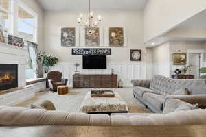 Carpeted living area featuring a decorative wall, a wainscoted wall, a glass covered fireplace, a chandelier, and a towering ceiling